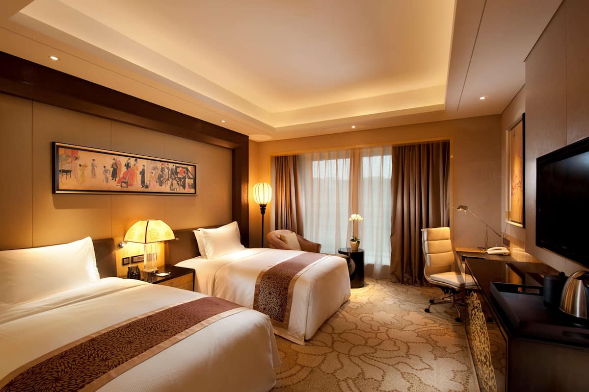 A hotel room with two beds, a desk, a TV, and a large painting on the wall.