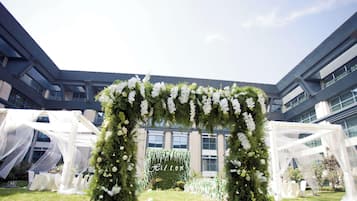 Een buitenbruiloftbogen met witte bloemen en begroeiing, voor een moderne gevel.