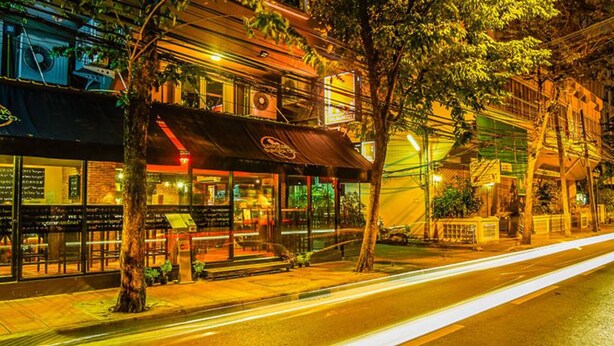 A street view at night with a restaurant featuring outdoor seating and a visible awning. - The Inn Saladaeng (Bangkok)
