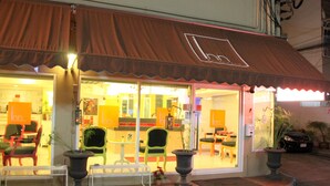 A restaurant with a brown awning, outdoor seating with chairs and tables, and potted plants. - The Inn Saladaeng (Bangkok)