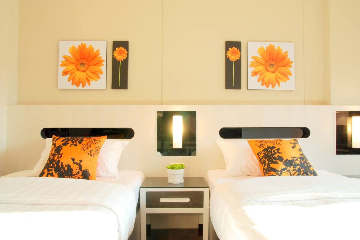 Een hotelkamer met twee bedden, elk voorzien van een witte spreidek en passende kussens. Boven de bedden hangen twee bloemschilderingen.