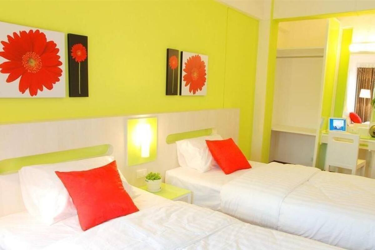 Een hotelkamer met twee bedden, een heldergele muur en bloemrijk kunstwerk in rood.