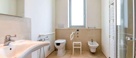 A modern bathroom with a sink, toilet, bidet, and a glass shower enclosure.