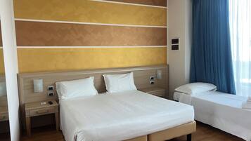 Une chambre d’hôtel avec un grand lit, un lit plus petit, une table de chevet et une fenêtre avec des rideaux.