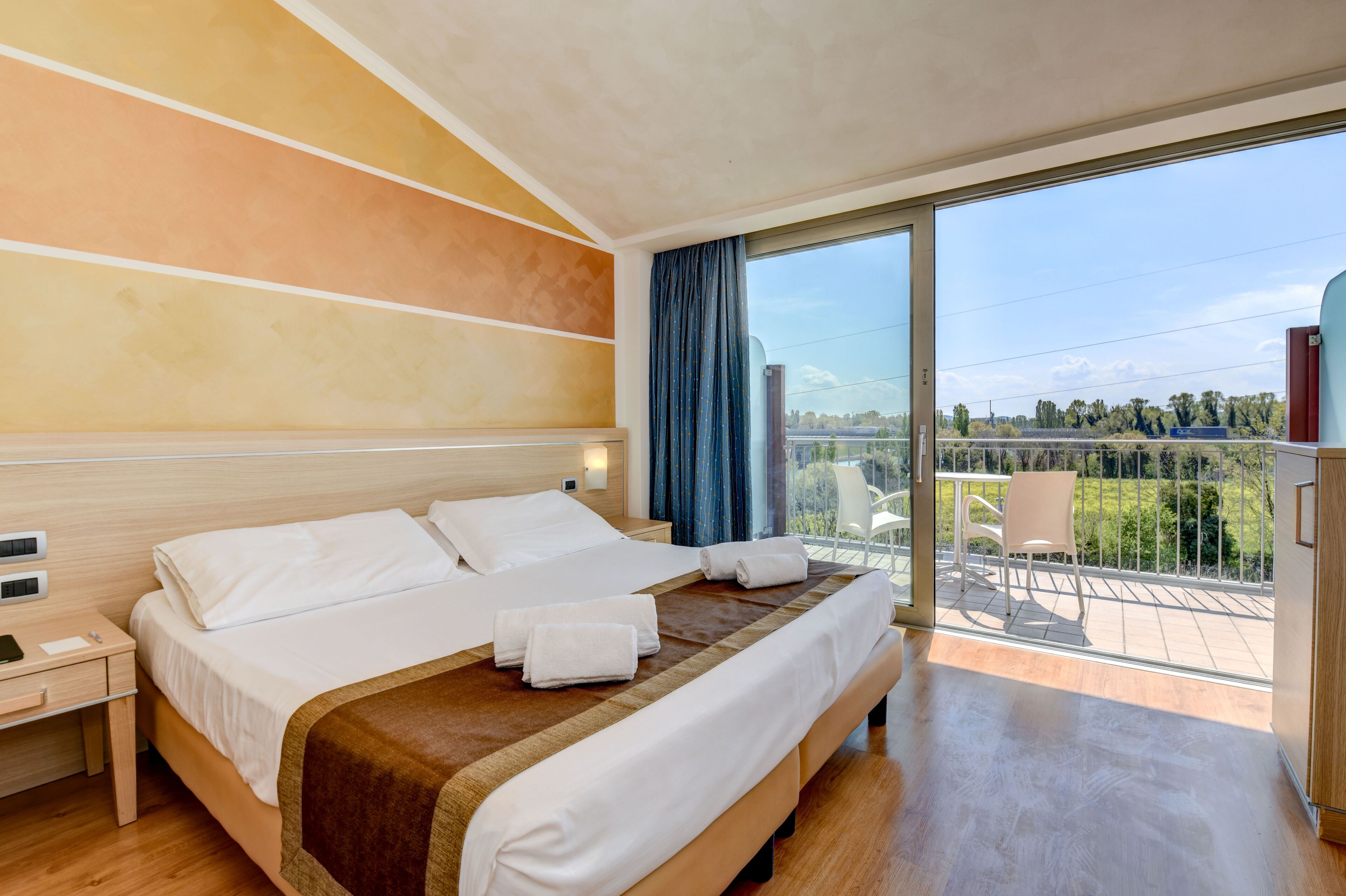 A hotel room with a large bed, a nightstand, a desk, and a view of the outdoors.