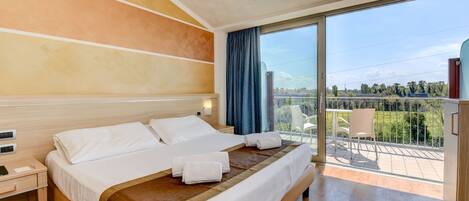 A hotel room with a large bed, a nightstand, a desk, and a view of the outdoors.