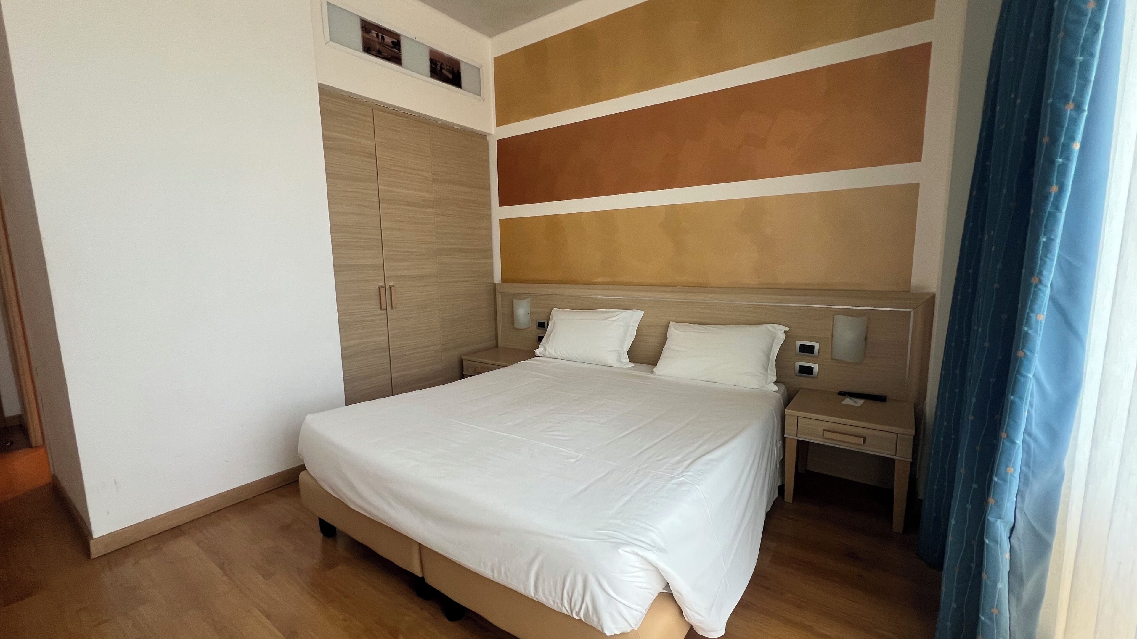 A bedroom with a bed, bedside tables, a wardrobe, and a wall-mounted light fixture.