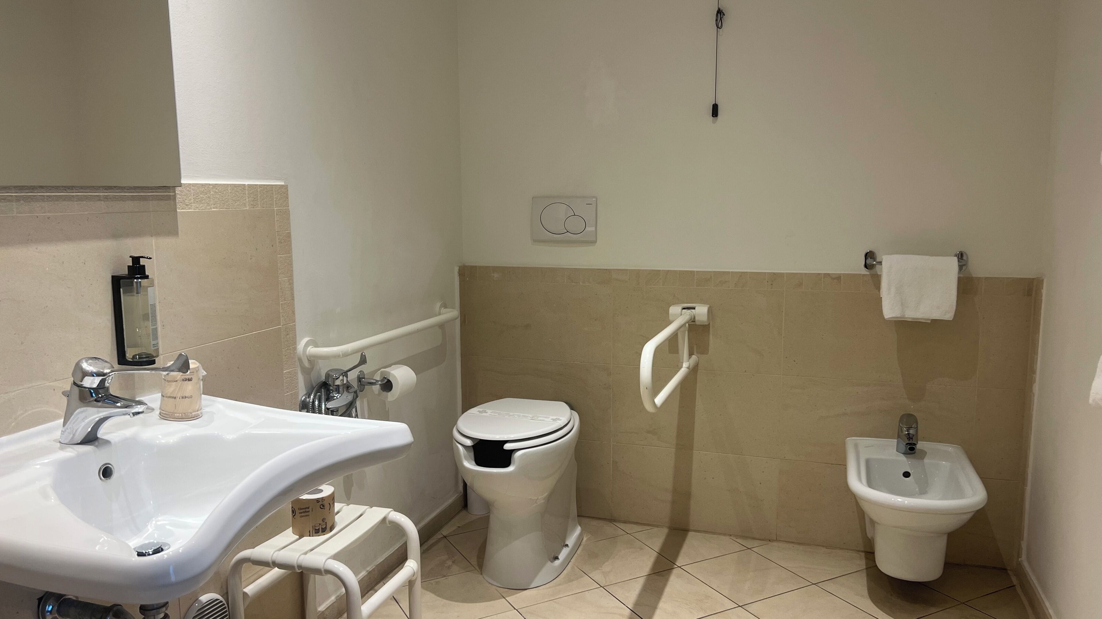 Een badkamer met een wastafel, toilet, bidet en handgrepen.
