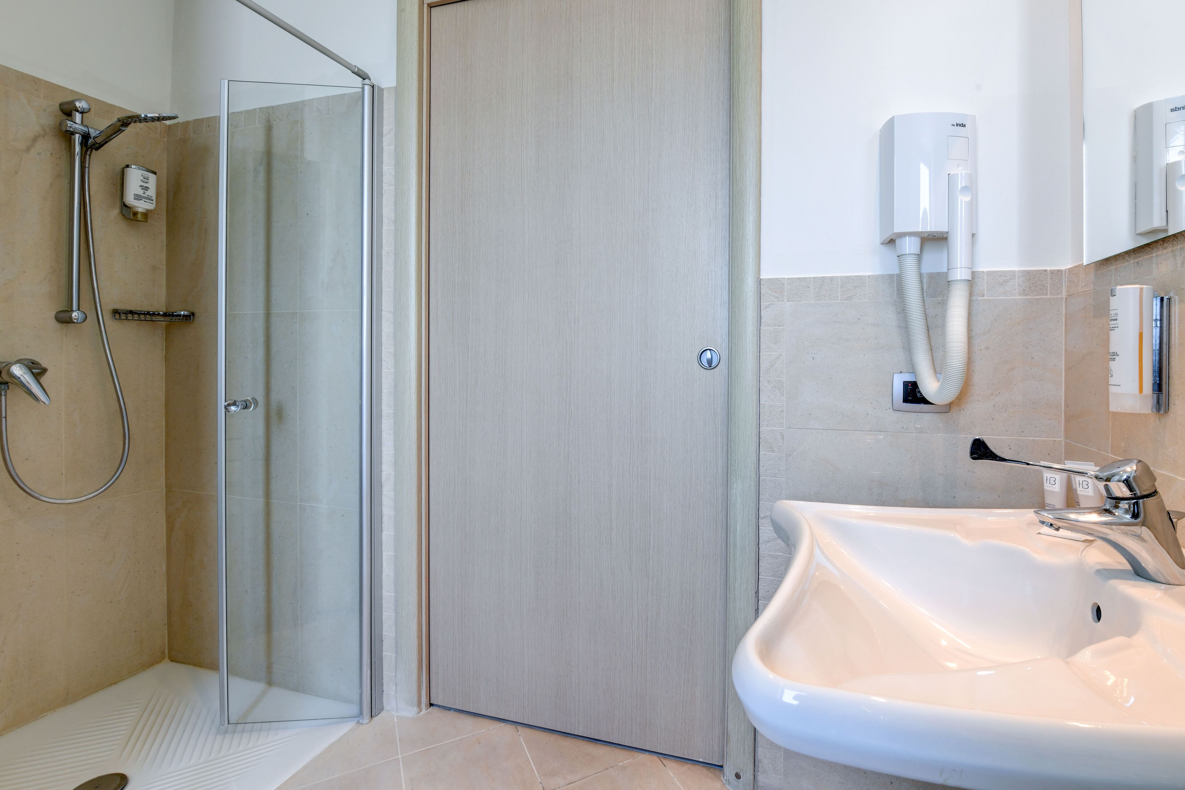 Un baño moderno con ducha acristalada, lavamanos blanco y secamanos de pared.
