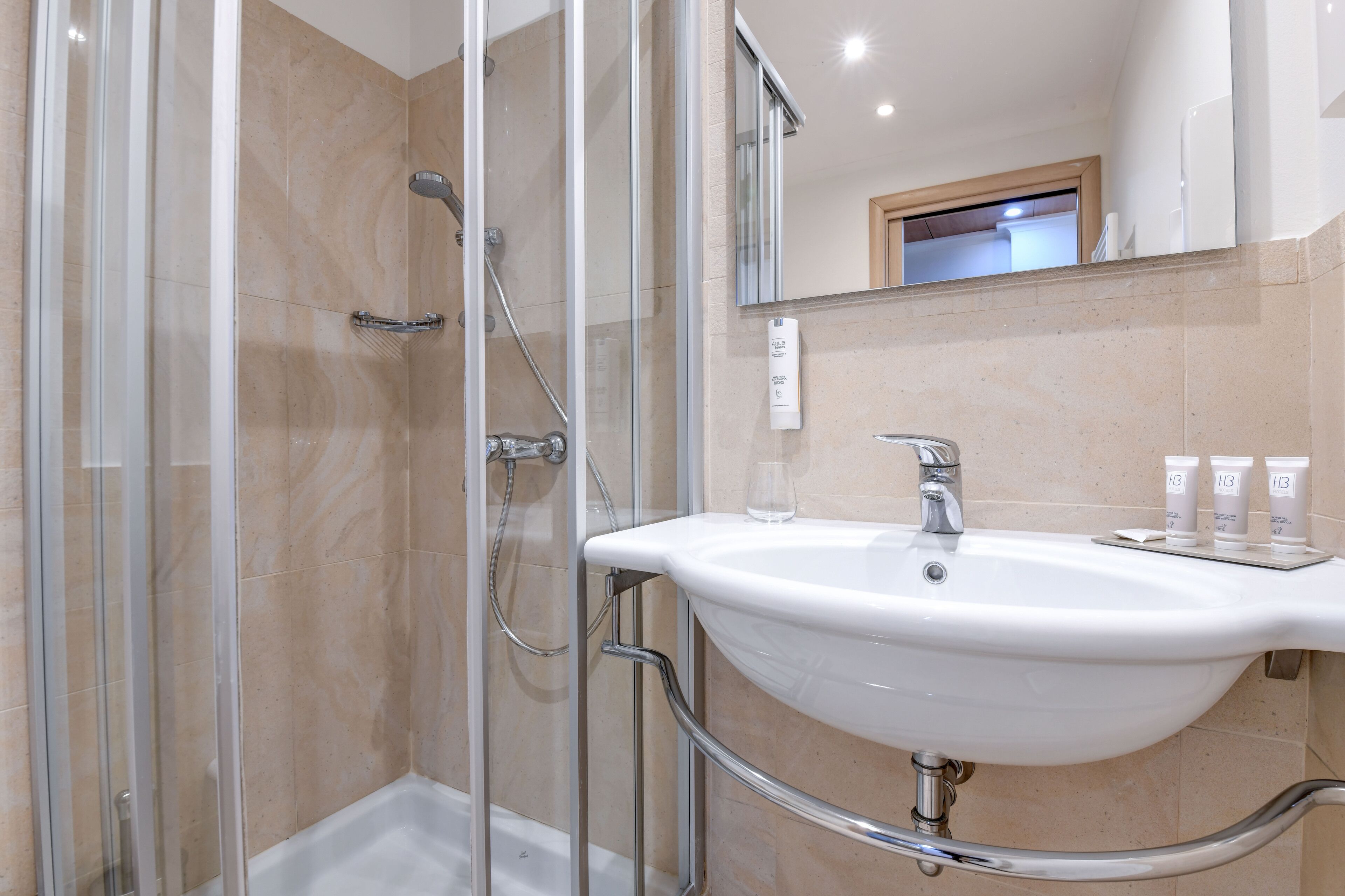 A modern bathroom with a glass shower enclosure, a white sink with chrome fixtures, and a mirror above the sink.