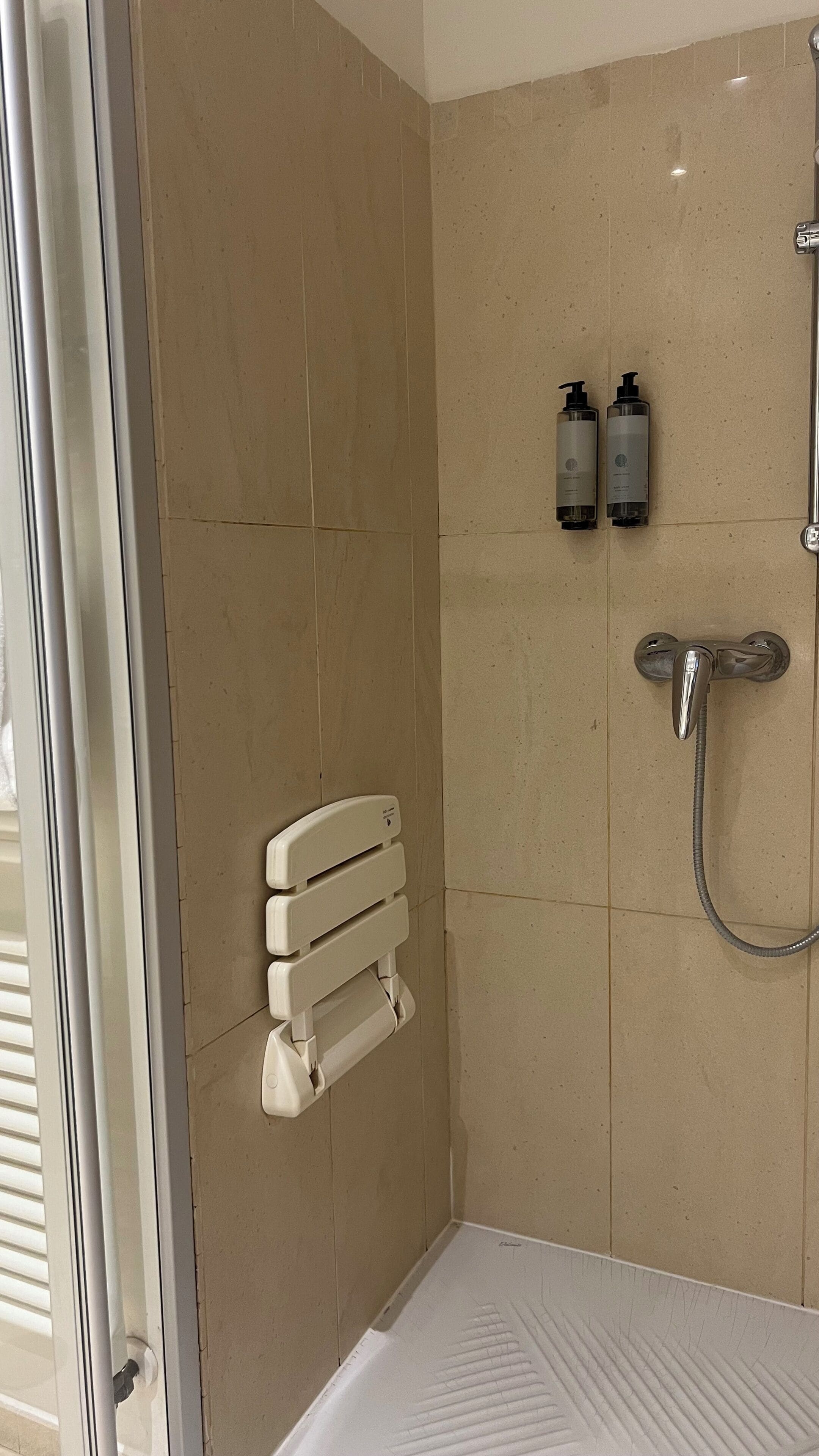 A shower with a handheld showerhead, a handheld showerhead, and two bottles of shampoo.