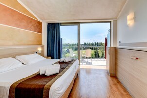 A hotel room with a large bed, a wooden floor, a balcony with a view, and a sliding door.