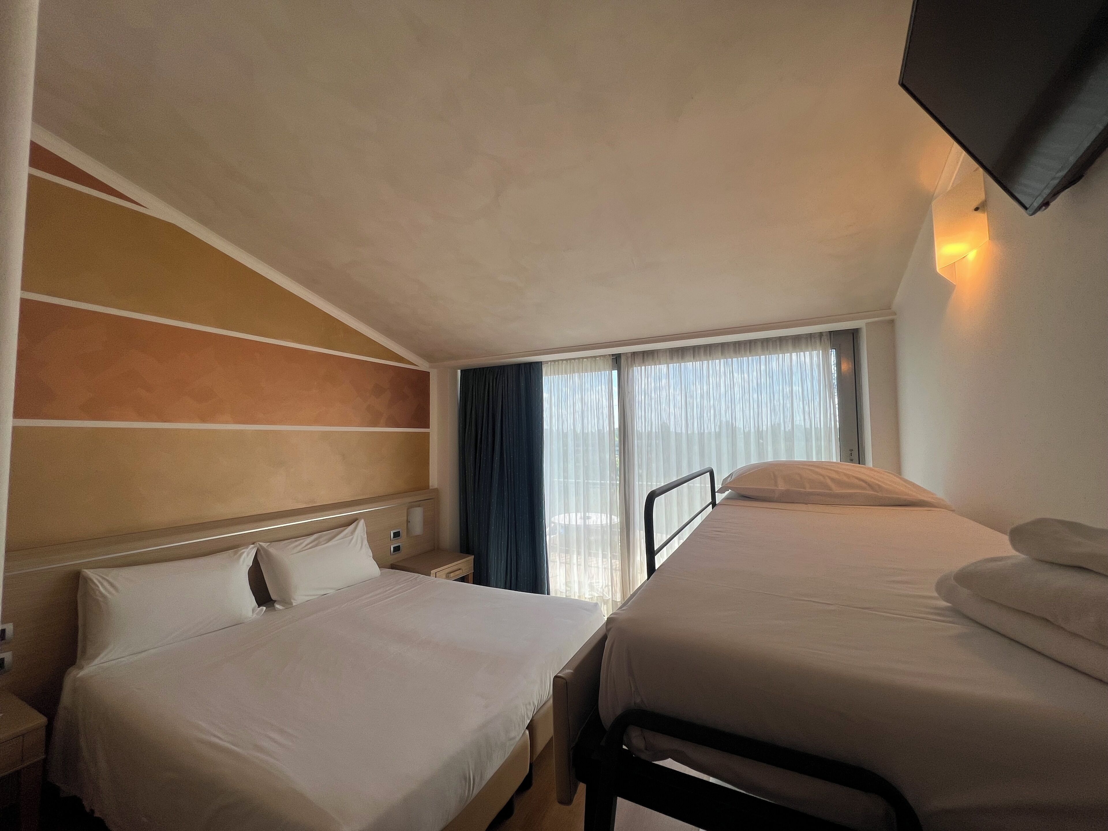 Een hotelkamer met twee bedden, een nachtkastje, een televisie en een raam met gordijnen.