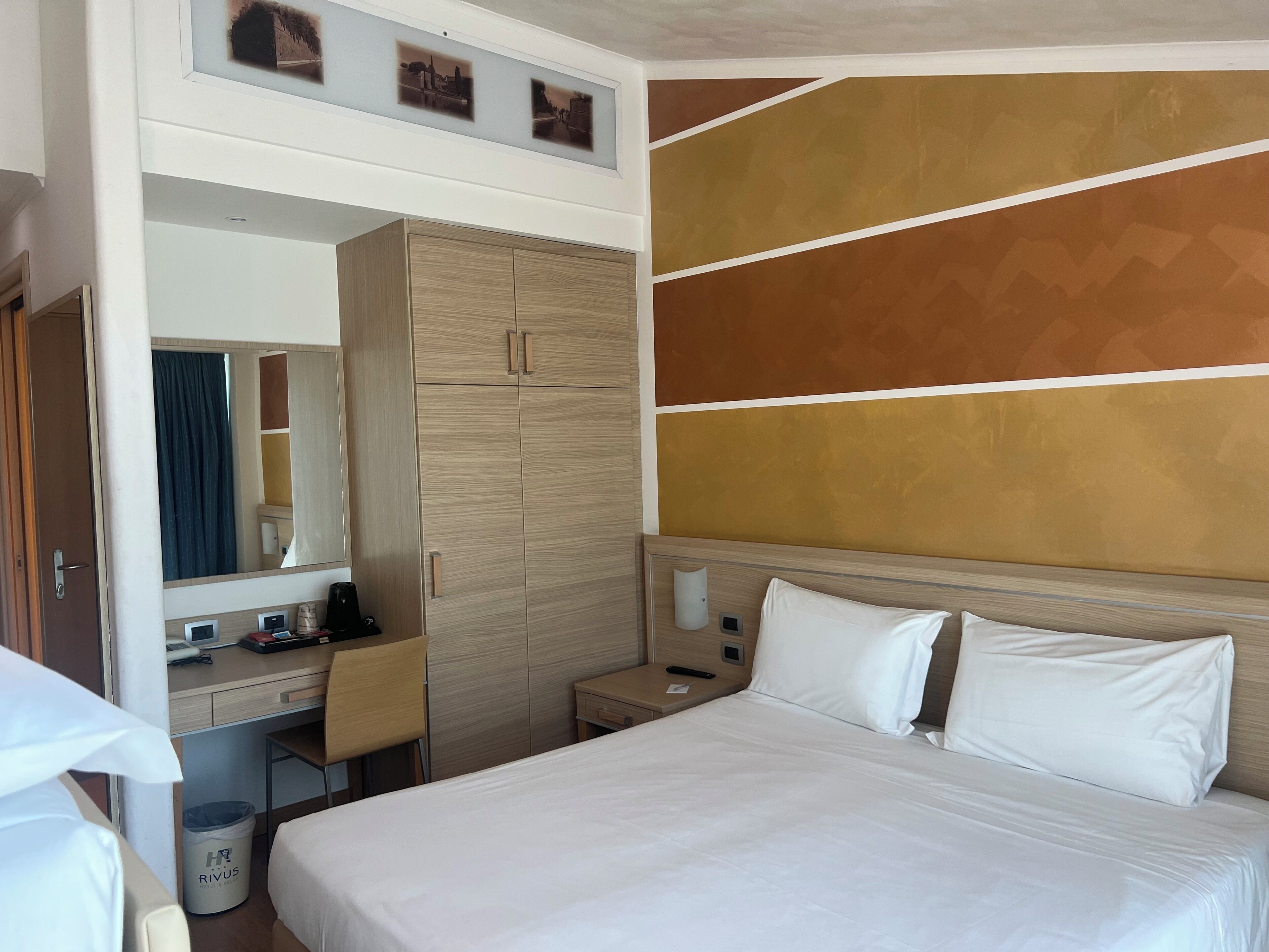 Une chambre d’hôtel comprenant un lit, un bureau, une armoire, un miroir et un mur orné d’un motif géométrique.