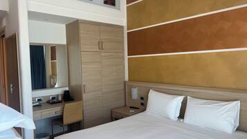 A hotel room with a bed, a desk, a wardrobe, a mirror, and a wall with a geometric design.