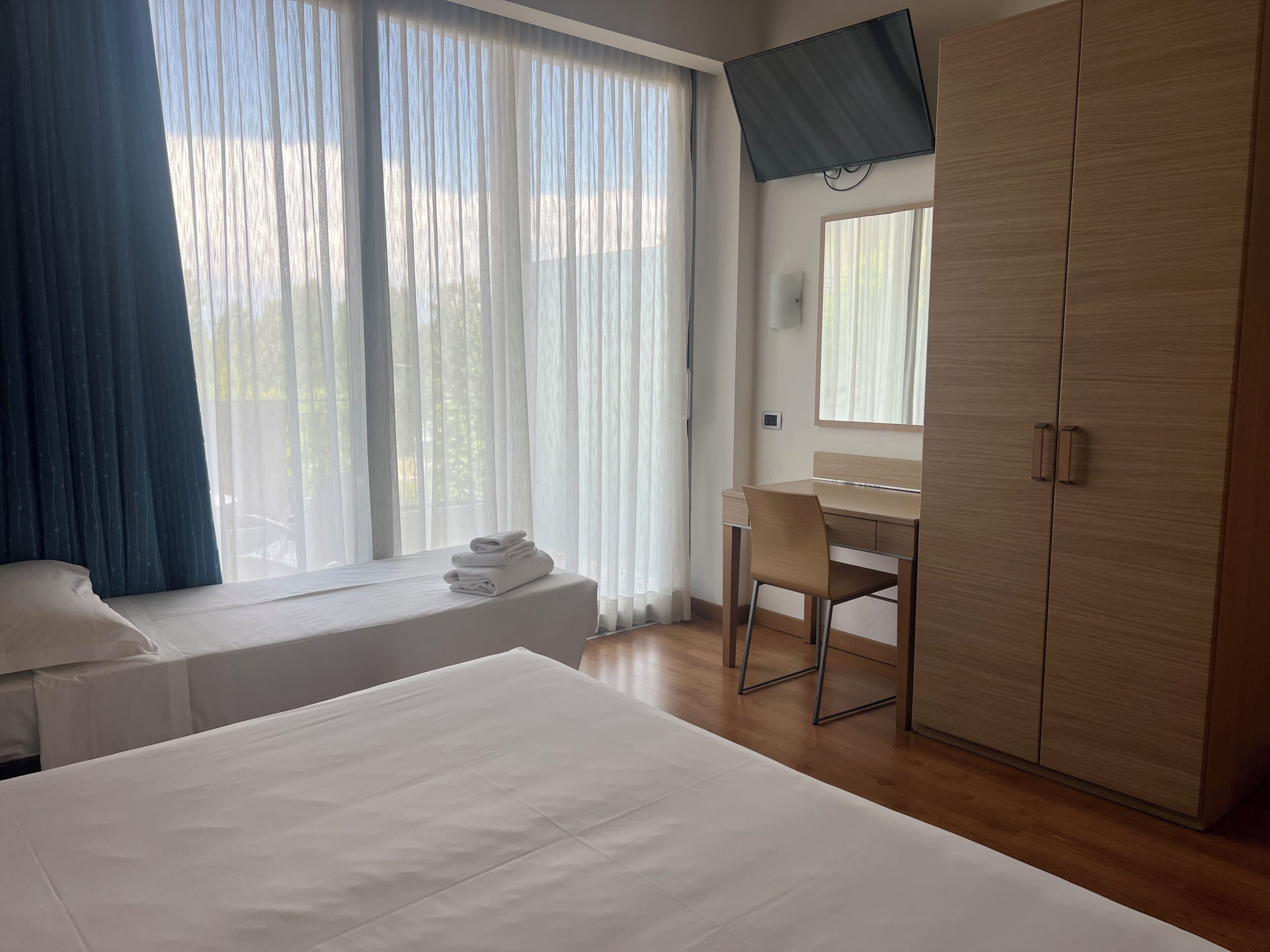 A hotel room with a bed, a desk, a wardrobe, and a window with curtains.