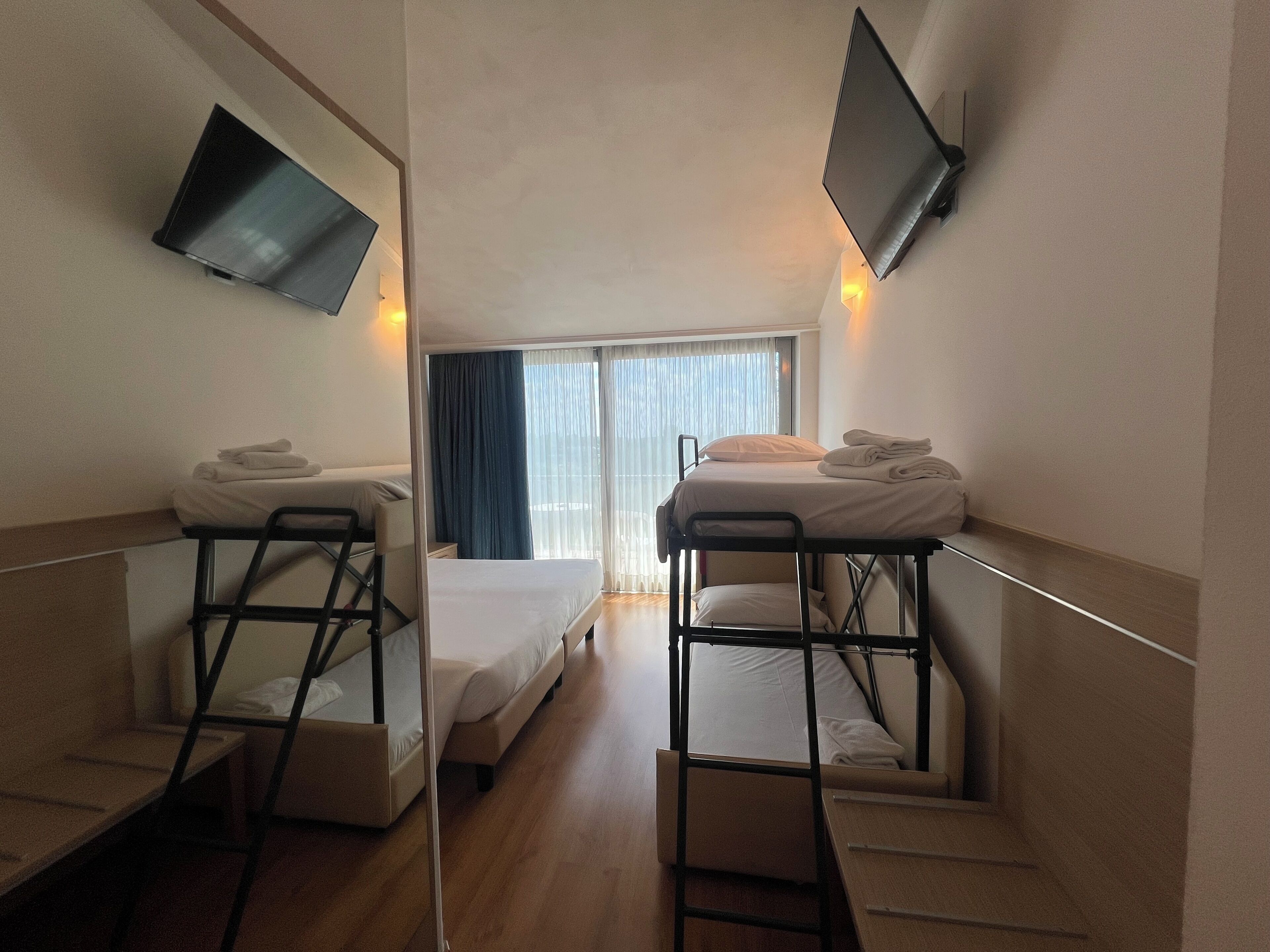A hotel room with bunk beds, a flat-screen TV, and a window with curtains.