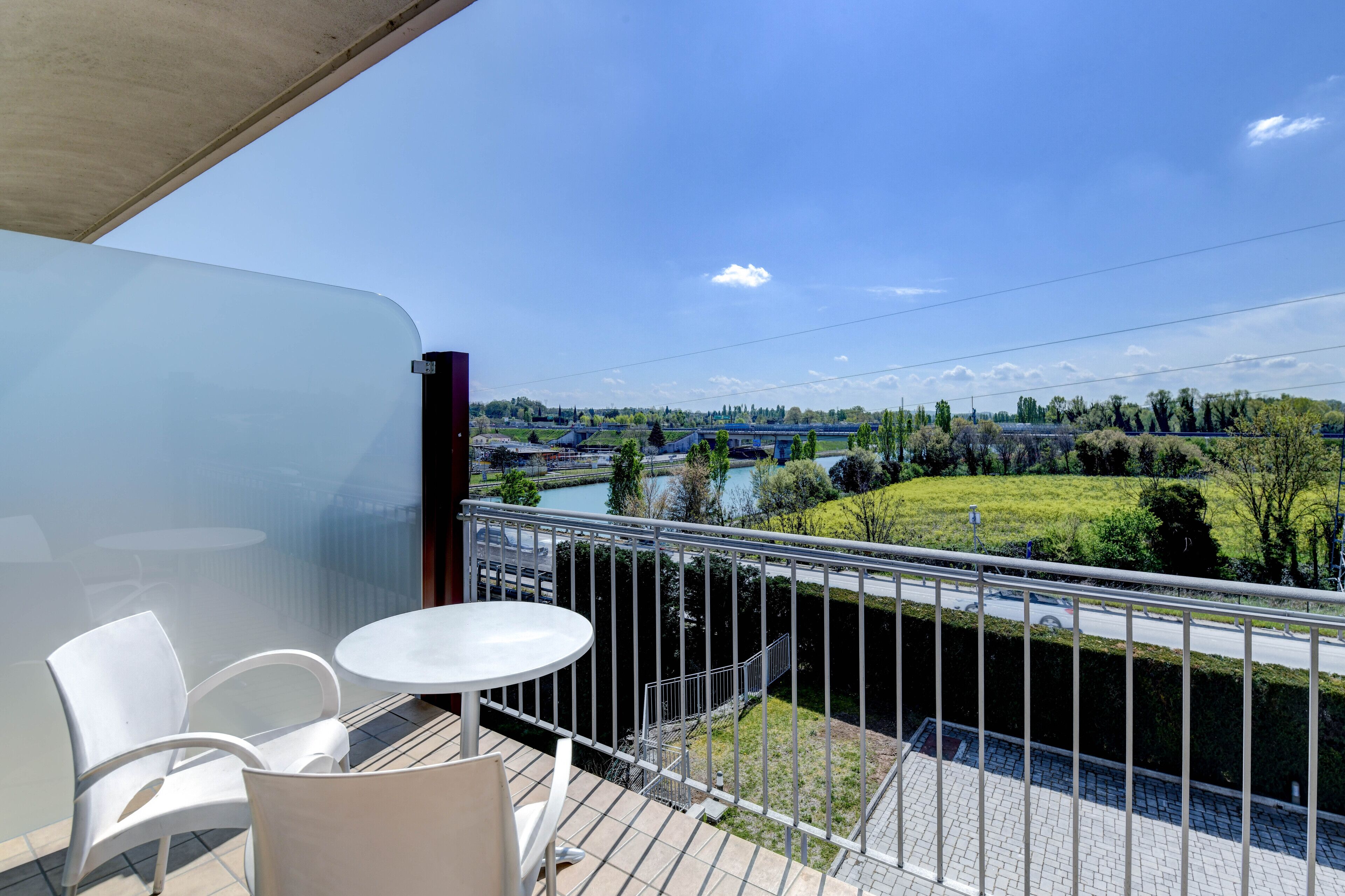 A balcony with a table and chairs, overlooking a river and greenery.