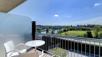 A balcony with a table and chairs, overlooking a river and greenery.
