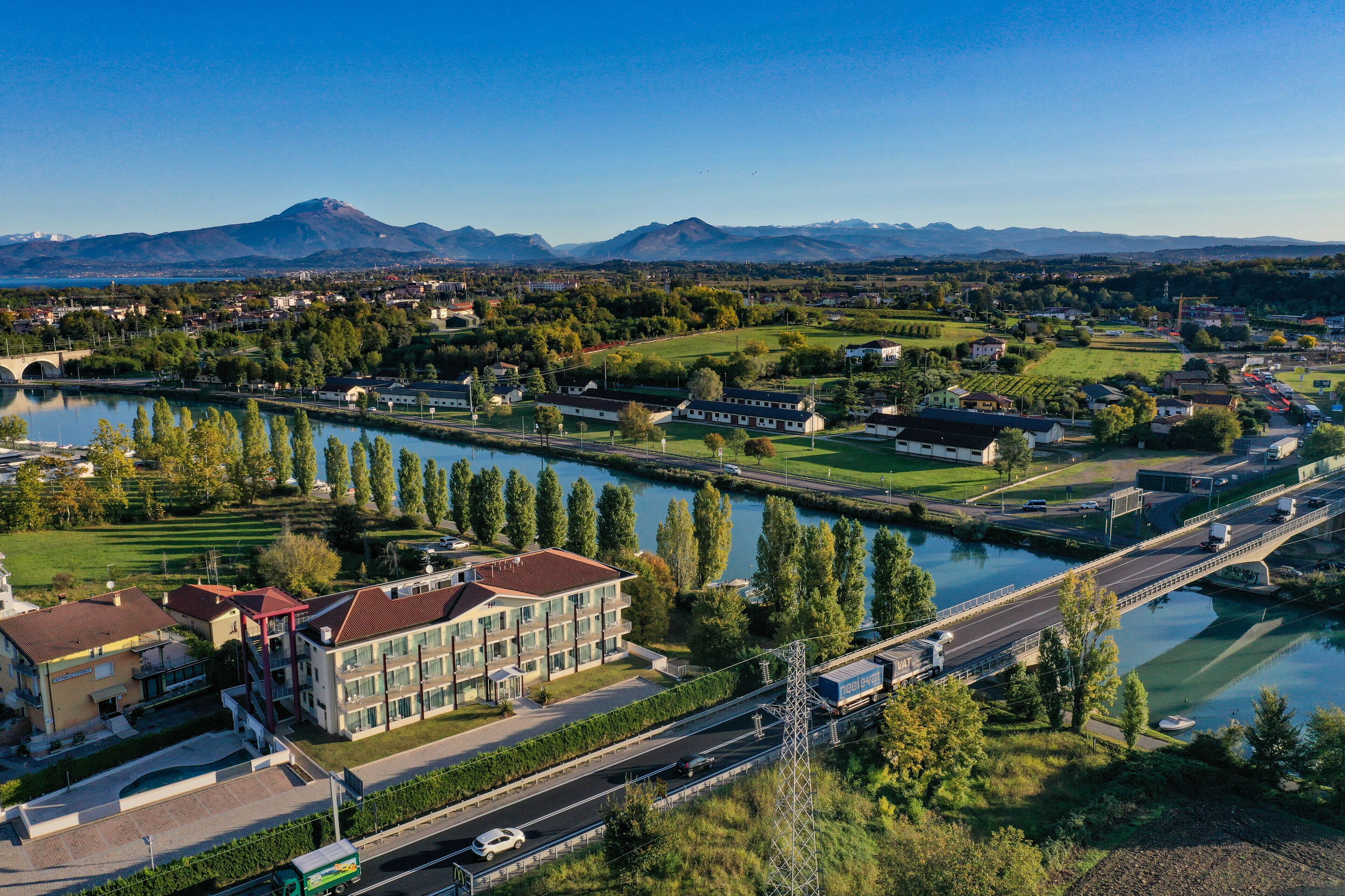 A riverside hotel with a view of the river, a bridge, and mountains in the background.