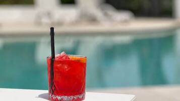 A glass of red drink with a straw on a white table by a pool.