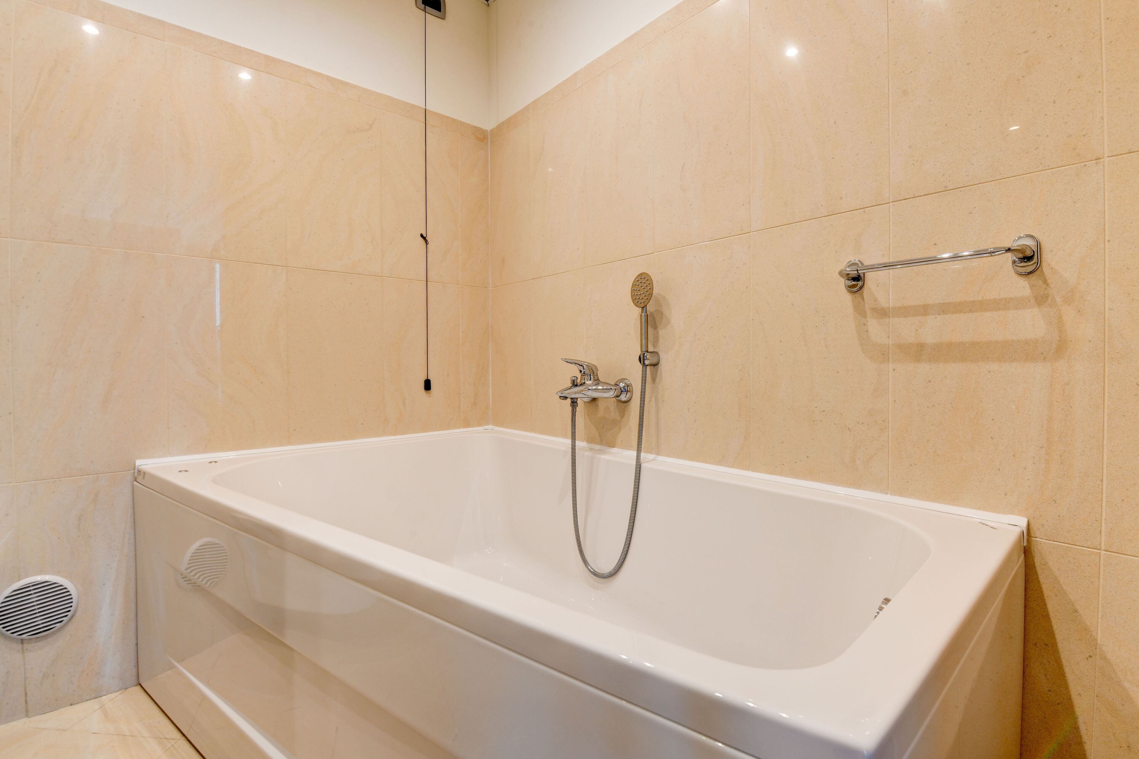 A modern bathroom with a white bathtub, a handheld showerhead, and a grab bar on the wall.