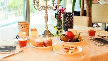 Une table de petit-déjeuner avec des viennoiseries, des fruits et des boissons, un chandelier et un vase décoratif.