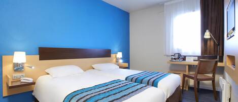 Habitación de hotel con dos camas, un escritorio, una silla y un ventanal con cortinas.