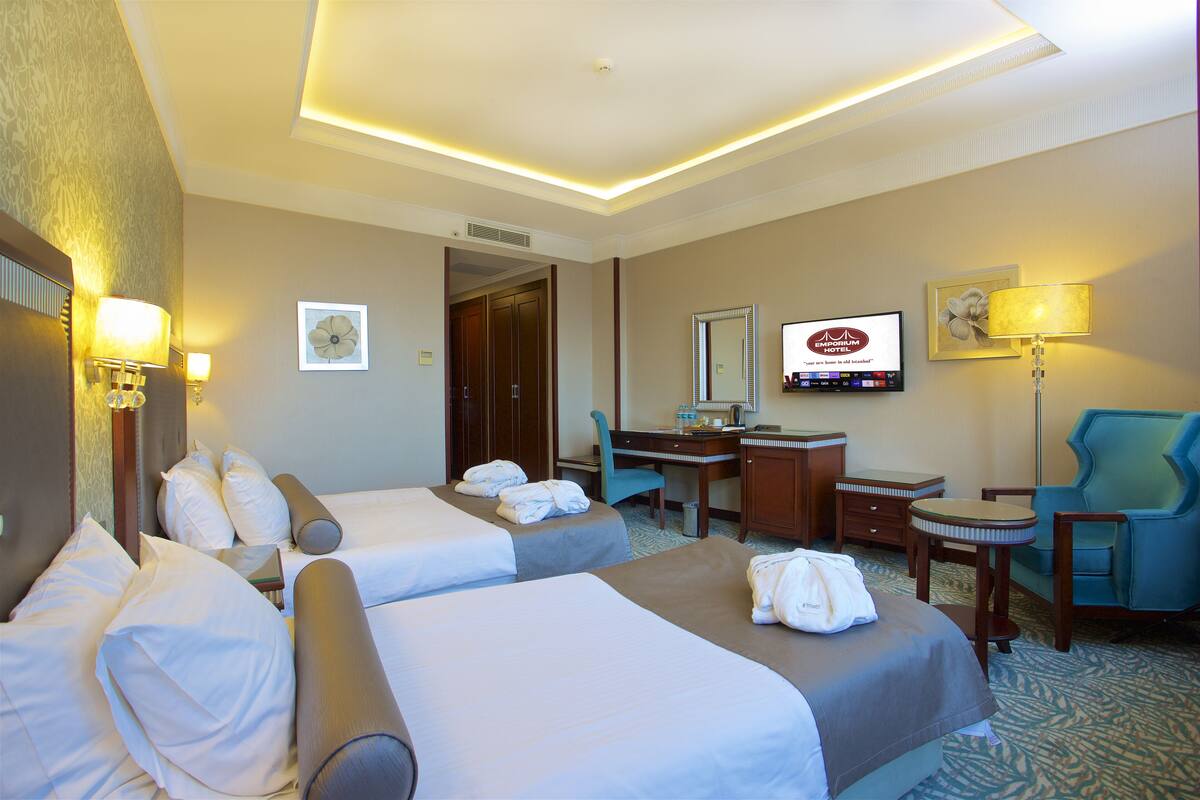 A hotel room with two beds, a desk, a chair, a television, and a bathroom.