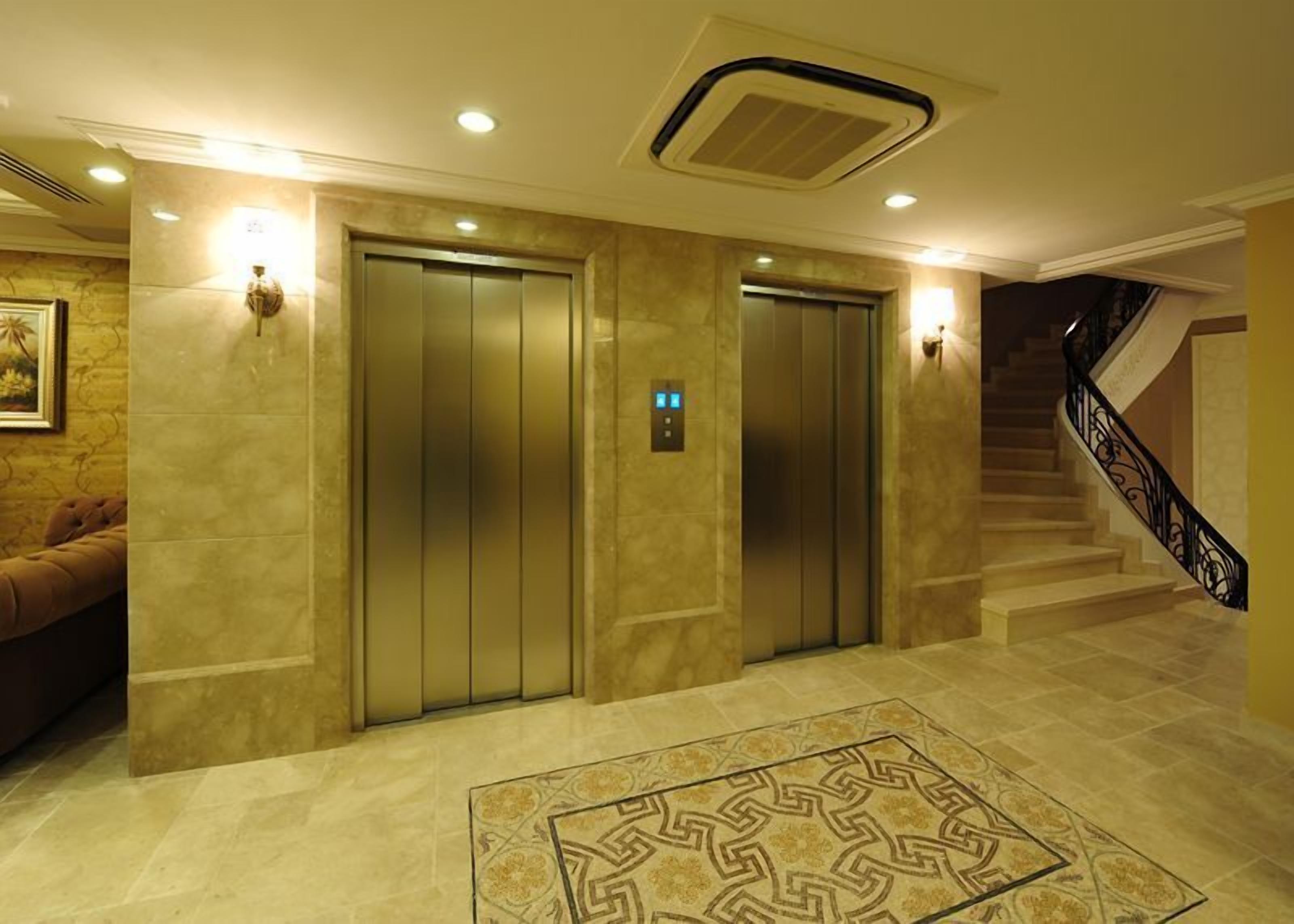 A lobby with two elevators, a patterned carpet, and a staircase with a black railing.