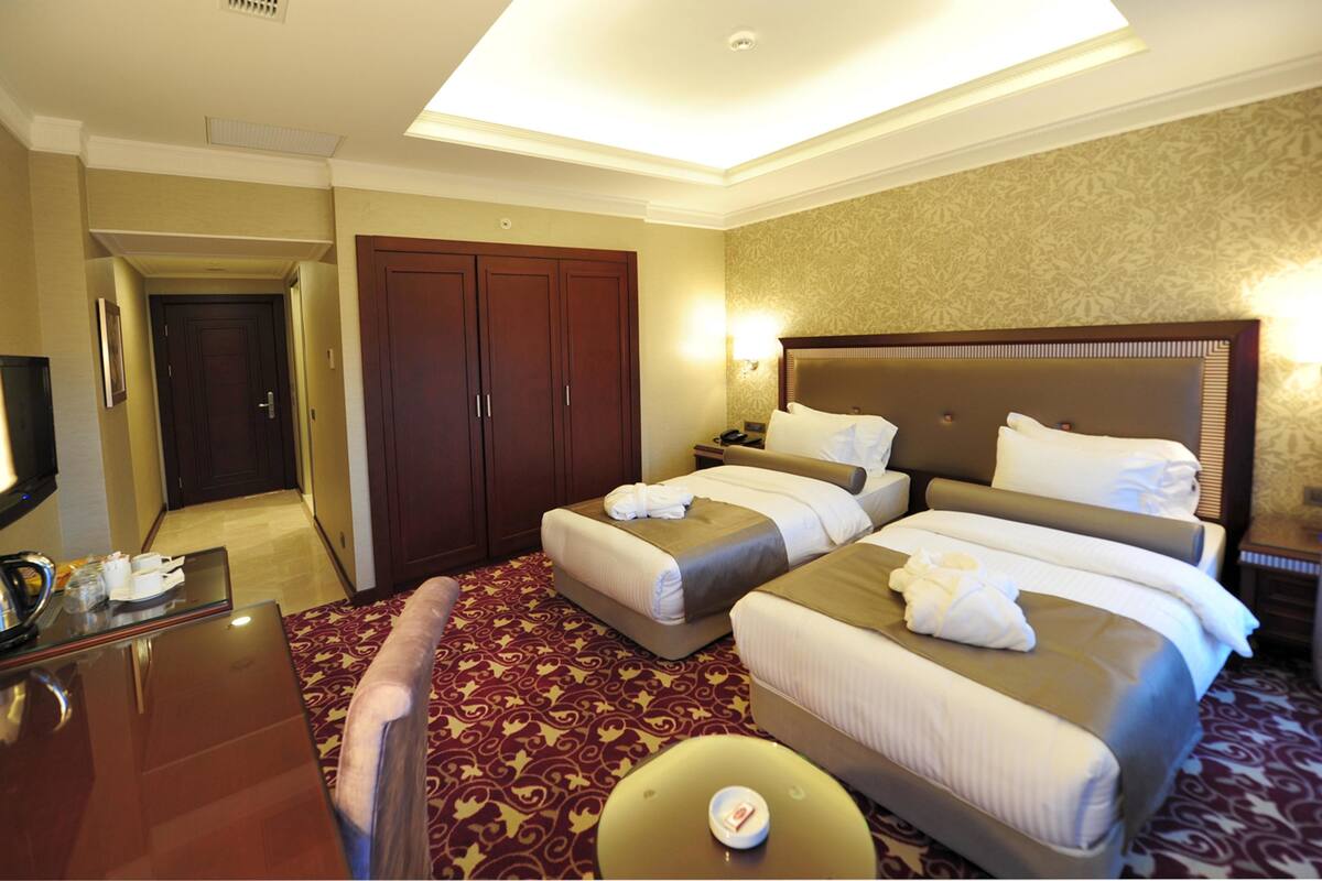A hotel room with two beds, a desk, a chair, a wardrobe, and a bathroom door.