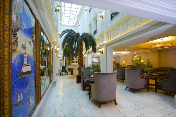 A spacious lobby with high ceilings, a central palm tree, and a seating area with armchairs and tables.