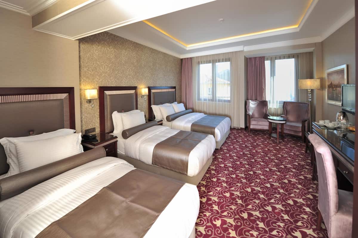 A hotel room with three beds, a desk, a chair, and a television.