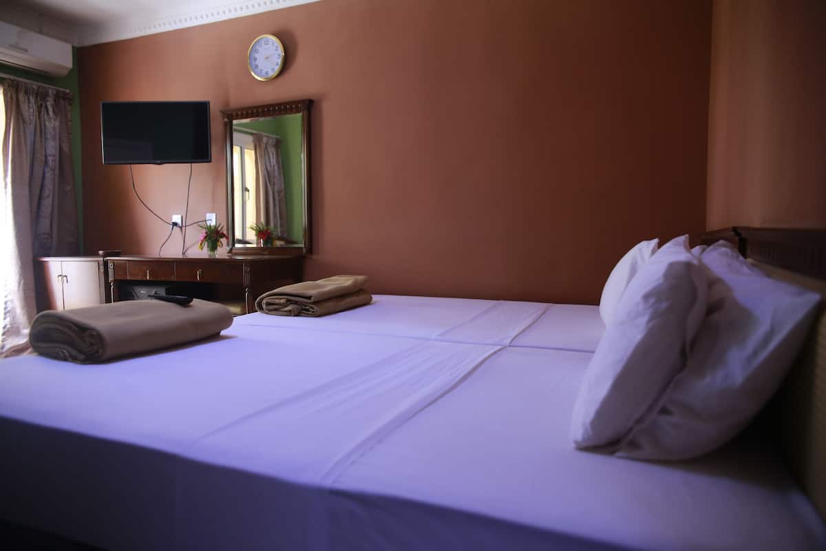 A hotel room with a bed, a flat-screen TV mounted on the wall, a clock, and a mirror.