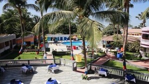 A poolside area with tables and chairs, palm trees, and a building in the background.