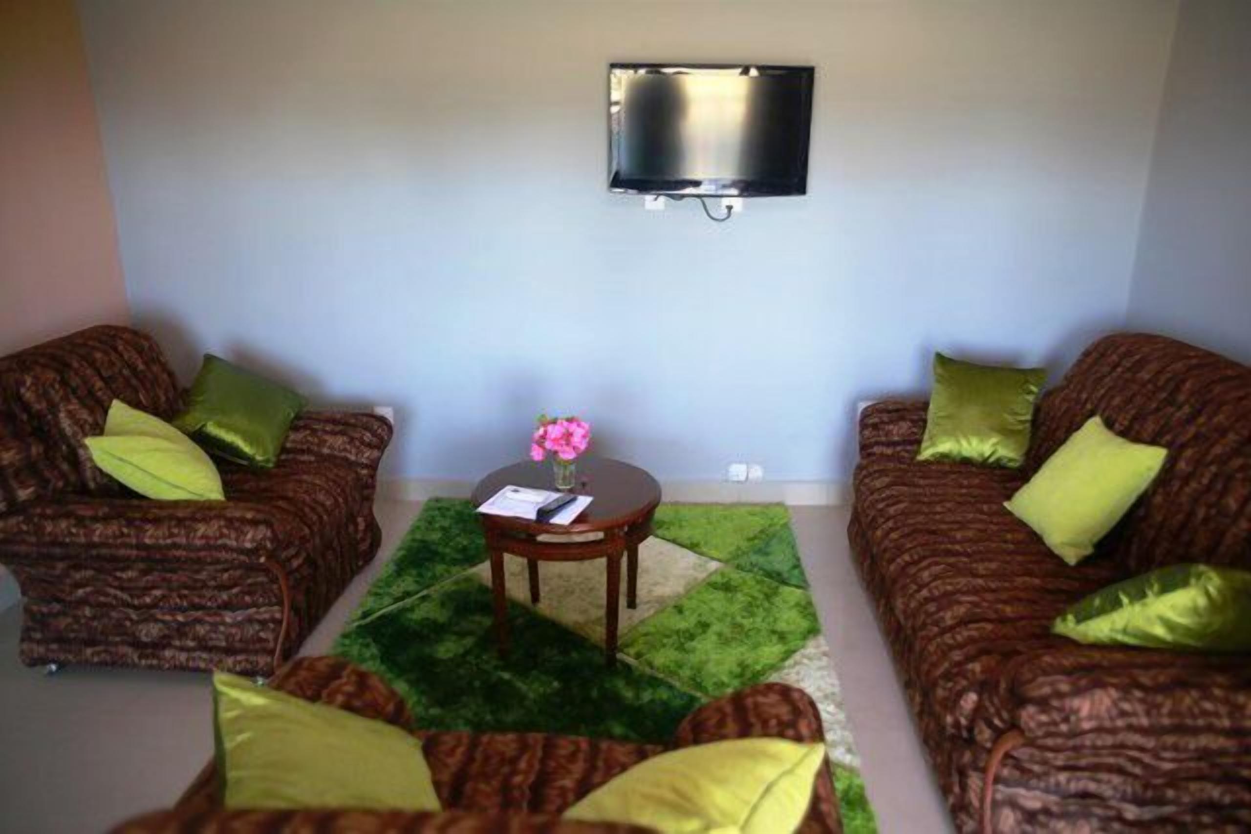 Una sala de estar con dos sofás estampados, una mesita redonda con un jarrón de flores y un televisor montado en la pared.