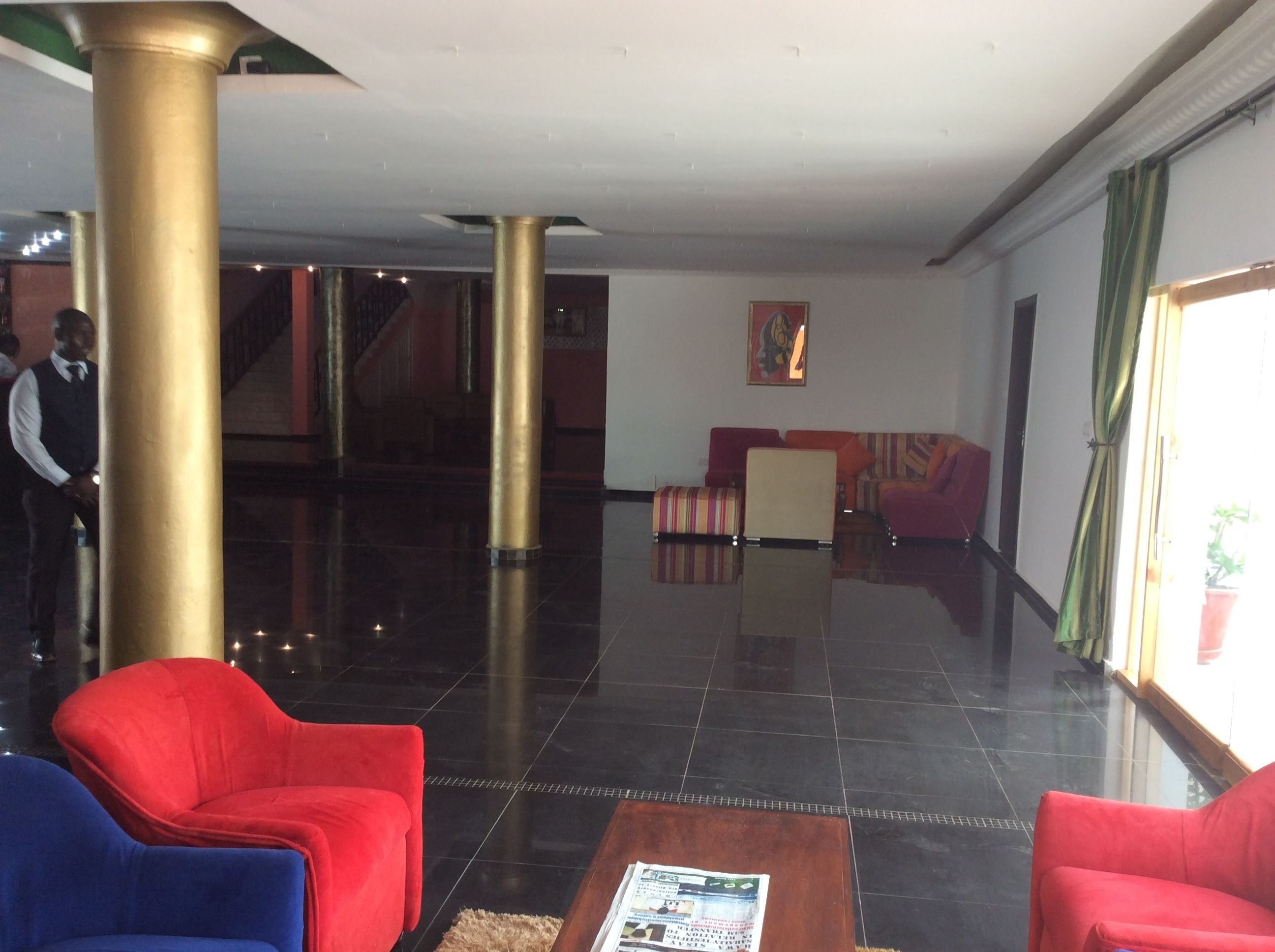 Un vestíbulo con piso pulido, una escalera y una zona de estar con sillas rojas y azules.