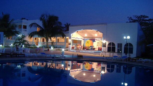 A hotel with a pool reflecting the building and palm trees.