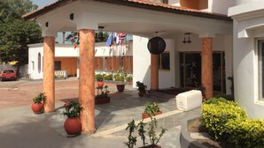 A building with a covered entrance, columns, and potted plants. Flags are displayed above the entrance.