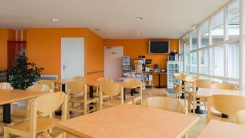 A dining area with wooden tables and chairs, a refrigerator, a microwave, and a television on the wall.