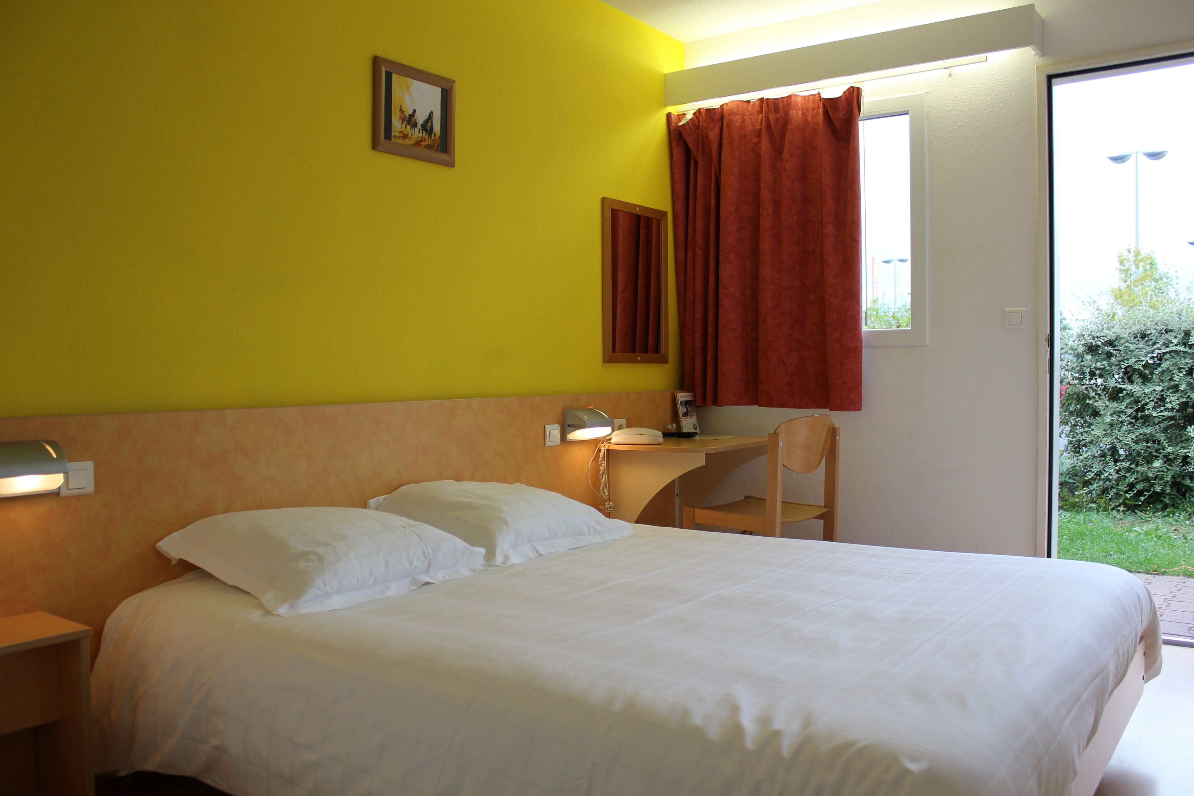 Habitación de hotel con cama, escritorio, silla y ventana con vistas a zonas verdes.