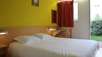Habitación de hotel con cama, escritorio, silla y ventana con vistas a zonas verdes.