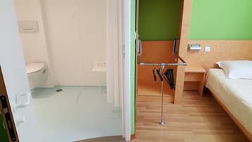 Hotellihuone, jossa on wc, sänky, vihreä seinä ja metallinen avainnaulakko.