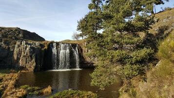 Una cascada que aboca a una bassa tranquil·la, envoltada de terreny rocos i vegetació escassa.