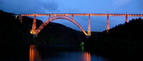 A large arched bridge with illuminated supports at dusk.