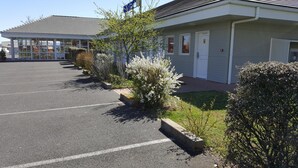A motel with a parking lot and a row of small shrubs in front. - The Originals Access, Hôtel St Flour (Andelat)