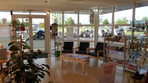 A spacious room with large windows, a reception desk, several chairs, and a small table. - The Originals Access, Hôtel St Flour (Andelat)