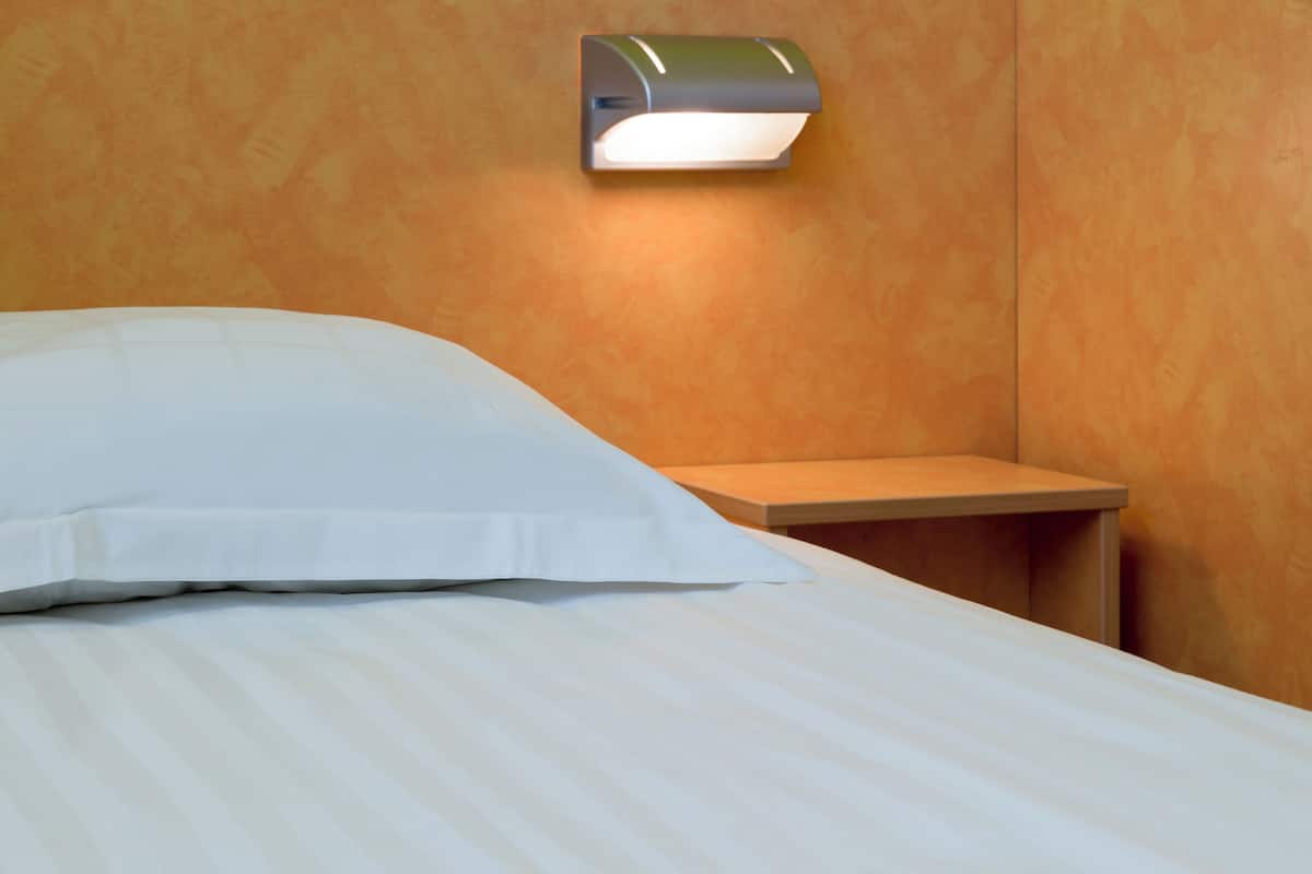 A bed with white linens, a nightstand with a lamp, and a wooden wall panel.