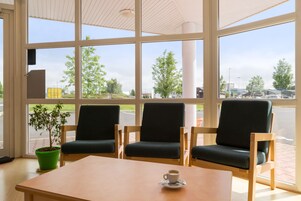 Un espacio de estar con tres sillas y una mesa, una planta en maceta, y vistas al exterior.
