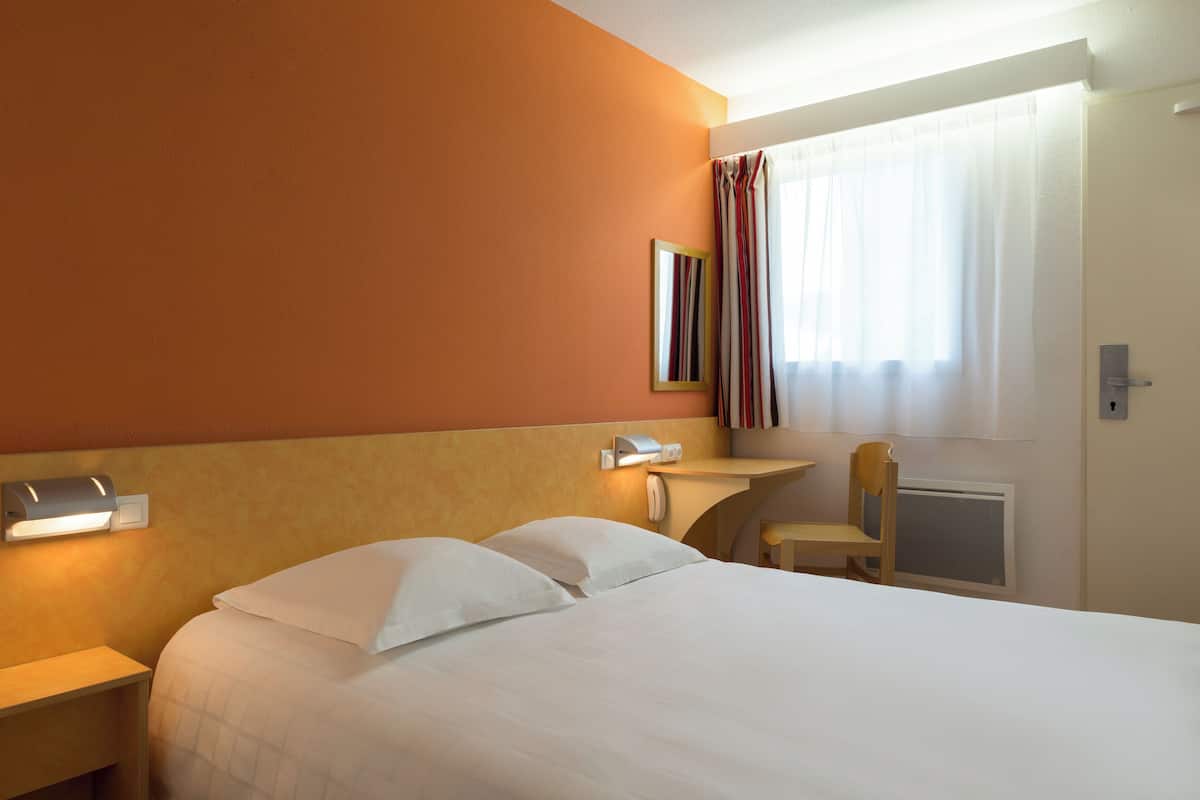 A hotel room with a bed, bedside table, lamp, chair, and a window with curtains.